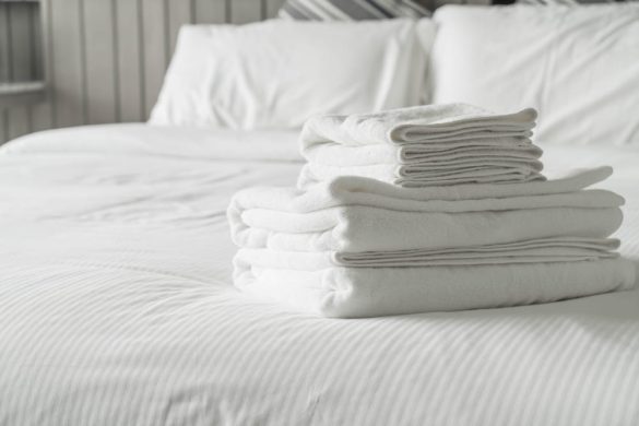 Une pile de serviettes de bain blanches fraîchement pliées posée sur une couette hôtellerie impeccable dans une chambre.