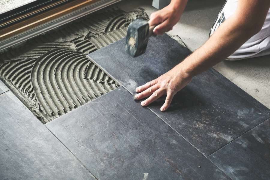 Un carreleur professionnel installe minutieusement de grands carreaux de sol sombres sur un lit de mortier peigné en vue de créer une salle de bain sécurisée.