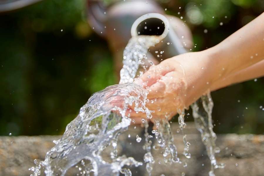 Une eau puissante jaillit d'un tuyau et éclabousse les mains d'une personne, illustrant une situation de pression d'eau trop élevée dans les installations.