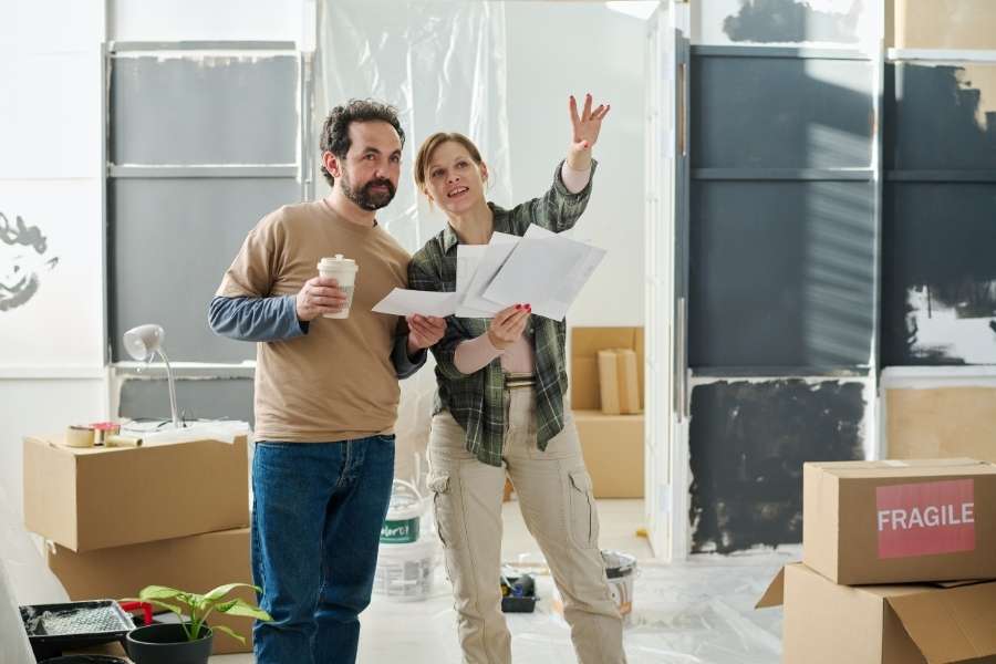 Un couple tenant des documents de chantier dans leur salon en rénovation avec une entreprise rénovation paris 5.