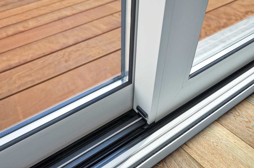 Gros plan sur les profilés robustes d'une baie coulissante menuiserie pvc grand passage et son rail de guidage étanche donnant sur une terrasse en bois